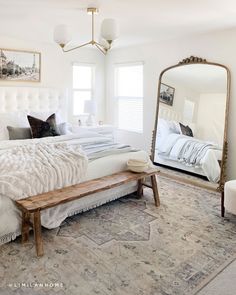 a large white bed sitting in a bedroom next to a mirror and footstool