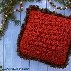 a red crocheted pillow sitting on top of a blue wooden floor next to a christmas tree