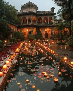 many lit candles are floating in the water near a building with arches and columns on it