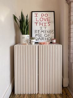 a white cabinet sitting next to a plant on top of a wooden floor