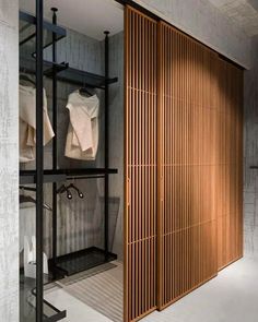 an open closet with wooden slats in the wall and clothes hanging on shelves behind it