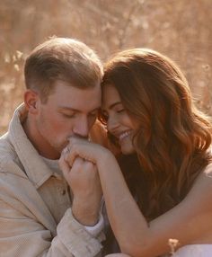 a man and woman sitting next to each other in the grass smiling at each other