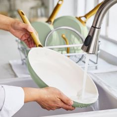 a person washing dishes in a kitchen sink with green plates and gold utensils