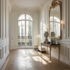 an elegant room with white walls and wood flooring, large mirror on the wall