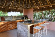 a kitchen with an island counter and stools under a thatched roof over looking trees