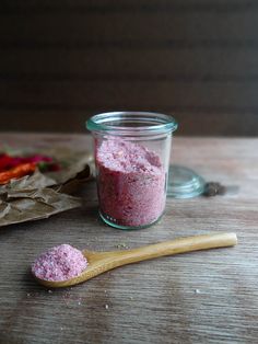 a jar filled with pink powder next to a wooden spoon on top of a table