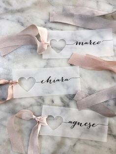 three place cards with hearts and ribbons tied to them on a marble countertop in the shape of heart