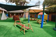 An outdoor childcare with grass floors and sheltered by black sail shades. There is a wooden climbing board at the back and a wooden plank in the middle. There is a tent on the left of the picture and an umbrella on a table on the opposite side. Outdoor Environment Childcare, Outdoor Environments Early Childhood, Outdoor Program Early Childhood, Wooden Planks, Bright Future