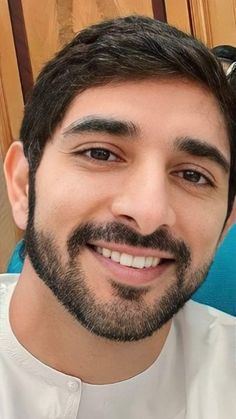 a close up of a person wearing a white shirt and beard smiling at the camera