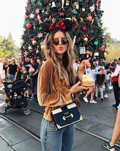 a woman standing in front of a christmas tree holding a bag and looking at the camera