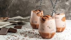 three glasses filled with ice cream and chocolate on top of a white table next to silverware