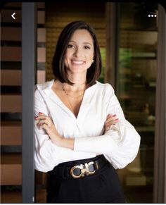 a woman with her arms crossed standing in front of a door wearing a white shirt and black pants