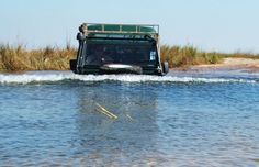 a truck is driving through the water in front of some grass and reeds,