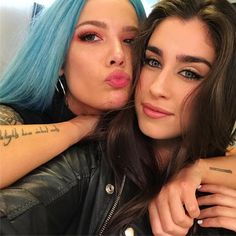 two women with blue hair and piercings are posing for the camera, one has her arm around the other's shoulder