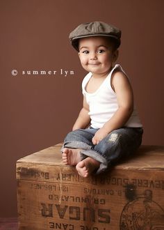 a young boy sitting on top of a wooden crate wearing a hat and jeans, smiling for the camera