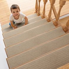 a young boy is crawling down the stairs on his carpeted stair treads, looking up at the camera