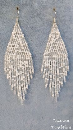 two pairs of white beaded earrings with fringes on the bottom and one pair hanging from