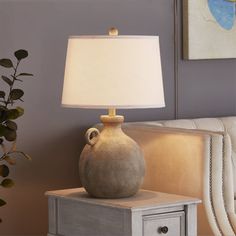 a table lamp sitting on top of a night stand next to a white couch in a living room