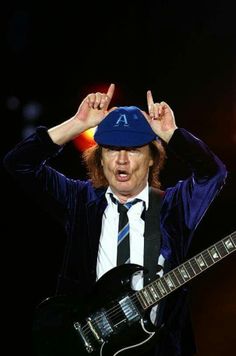 a man in a blue hat and tie holding his hands up to his head while playing an electric guitar