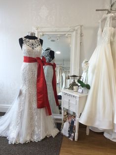 two wedding gowns are on display in front of a mirror, and one is wearing a red bow