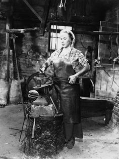 an old black and white photo of a woman working in a blacksmith