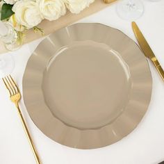 an empty plate on a white table cloth with gold cutlery and flowers in the background