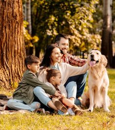 a family with two children and a dog sitting on a blanket in the grass under a tree