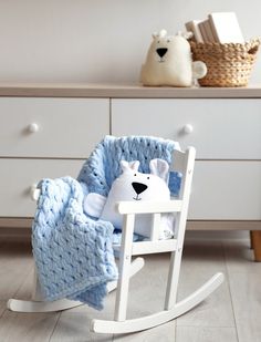 a white rocking chair with a blue blanket on it and a teddy bear in the middle