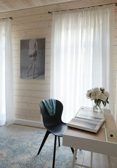 a chair and desk in front of a window with white drapes on the windowsill