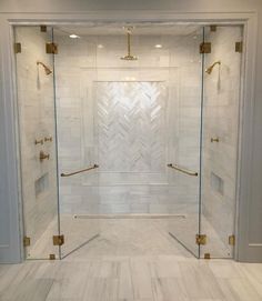 a walk in shower sitting next to a white tiled wall and floor with gold accents