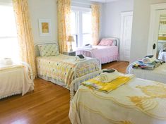 two beds in a room with wooden floors and yellow curtains on the windowsills