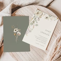 the wedding stationery is laid out on top of a wooden table with white and green flowers