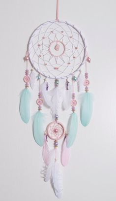 a white dream catcher hanging from the side of a wall with beads and feathers on it