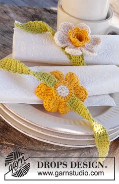 crocheted napkins with flowers on them sitting on a plate next to a cup and saucer