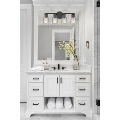 a white bathroom vanity with two lights above it and a vase on the counter top