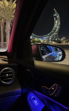 the view from inside a car at night with palm trees and lights in the background