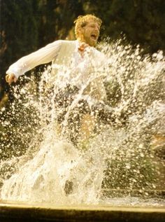 a man in white shirt jumping into water with his arms out and mouth wide open