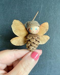 a hand holding a tiny pine cone angel ornament with blue eyes and brown wings