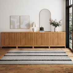 a room with a rug, mirror and two vases on the sideboard in it