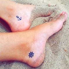 two people with anchor and compass tattoos on their feet sitting in the sand at the beach