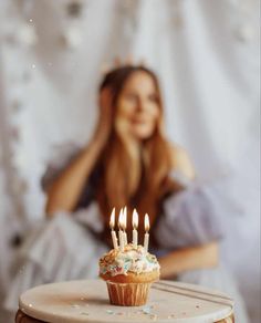 a cupcake with lit candles sitting on top of a table next to a woman