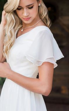 a woman in a white dress is looking down at her hair and wearing a pearl necklace