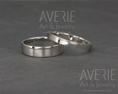 two silver wedding rings sitting on top of a gray surface with the words averie art & jewelry