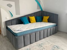 a bed that is in the middle of a room with blue and yellow pillows on it