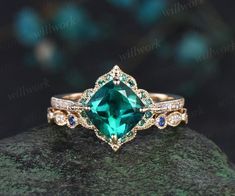 an emerald colored ring with blue and white diamonds on top of a green mossy rock