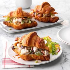 two croissants with meat, cheese and vegetables on them sitting on plates