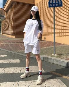 a woman standing on the street in front of a building wearing a white shirt and shorts