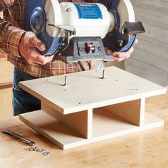 a man holding a circular saw on top of a piece of wood next to a table