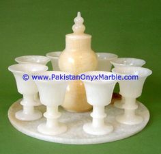 an assortment of white glass cups and vases on a marble tray with a green background