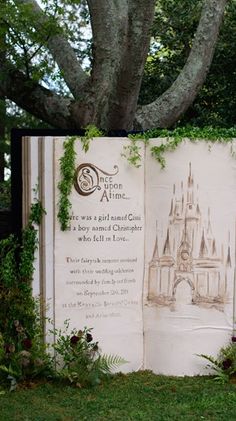 an open book sitting in the grass next to a tree and some flowers on it